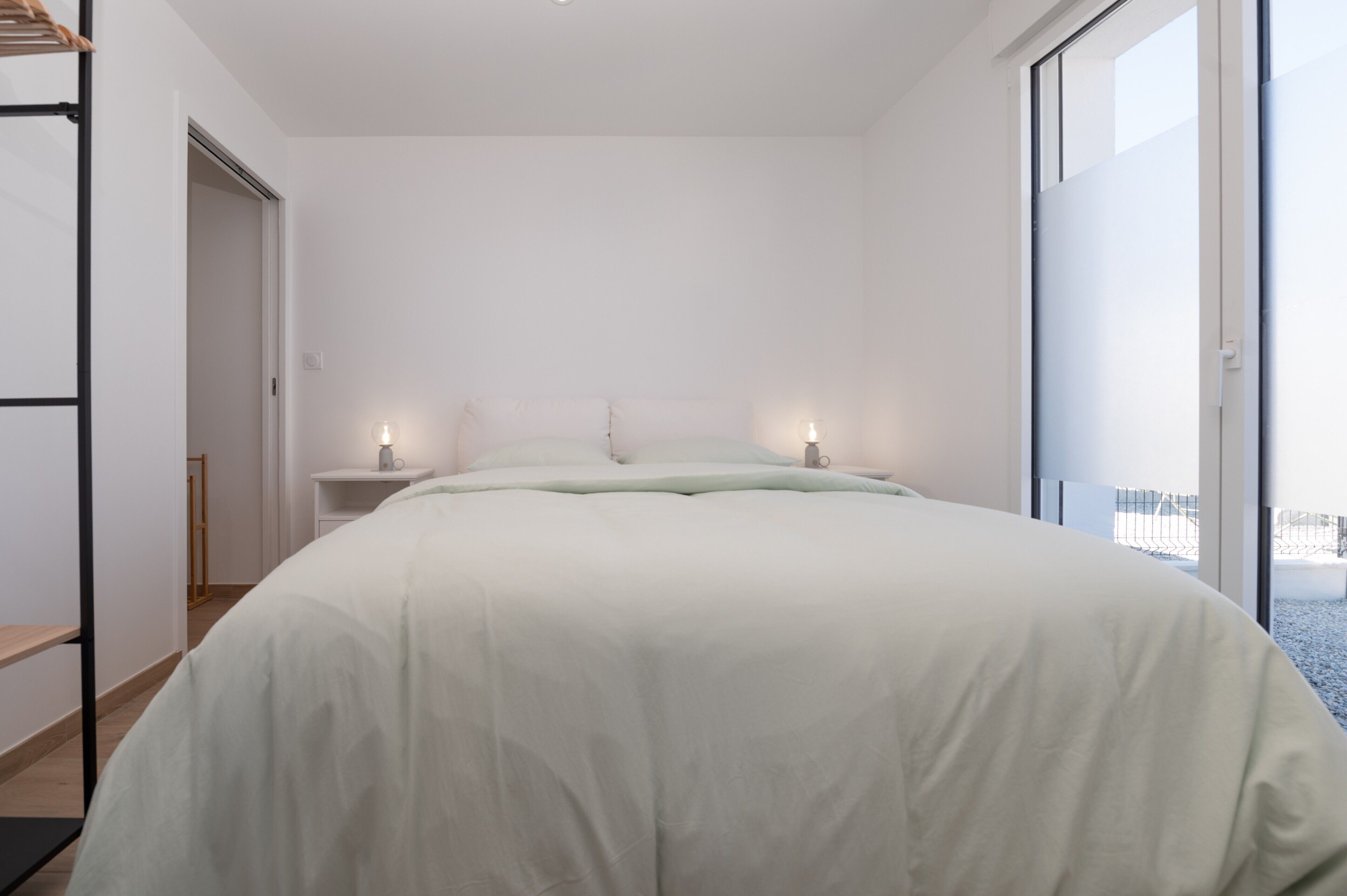 Une chambre à coucher avec un lit, des tables de chevet et une vue sur l’extérieur grâce à une grande fenêtre.