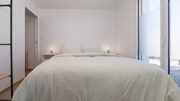 Une chambre à coucher avec un lit, des tables de chevet et une vue sur l’extérieur grâce à une grande fenêtre.