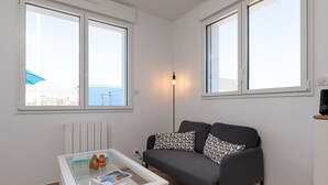 A modern living room with a grey sofa, a glass coffee table, and a view of the sea through large windows. - Bâbord, quiet artisan area, near port & beach, wifi, parking, towels & cleaning not included (Arzon)