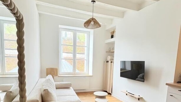 Un salon moderne avec un canapé, une table à manger en verre et un téléviseur fixé au mur.