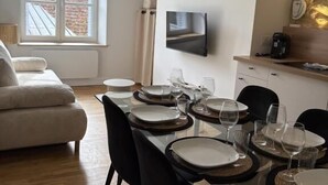Un espace repas moderne avec une table en verre pour six personnes, des chaises noires et un téléviseur fixé au mur.