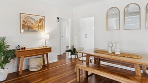 Ein modernes Wohnzimmer mit Holzboden, einem Holztisch, einem weißen Sofa, einem Beistelltisch mit Lampe und einem gerahmten Gemälde an der Wand.
