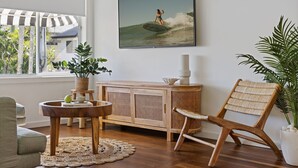 Ein Wohnzimmer mit Holzschrank, Korbstuhl, rundem Couchtisch und Topfpflanze.