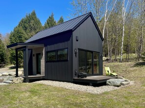 Uma cabana moderna com varanda coberta, janelas amplas e um deck.