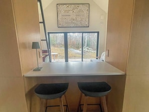 Cozinha compacta com janela, dois bancos e um objeto decorativo na parede.