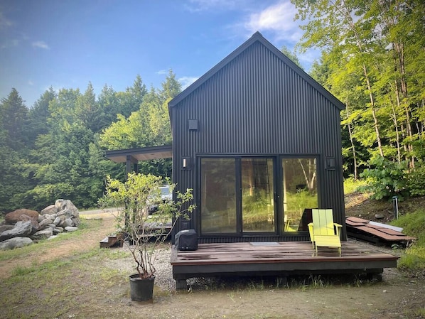 Uma cabana moderna com uma grande porta de vidro deslizante, um deck e uma pequena área de jardim.