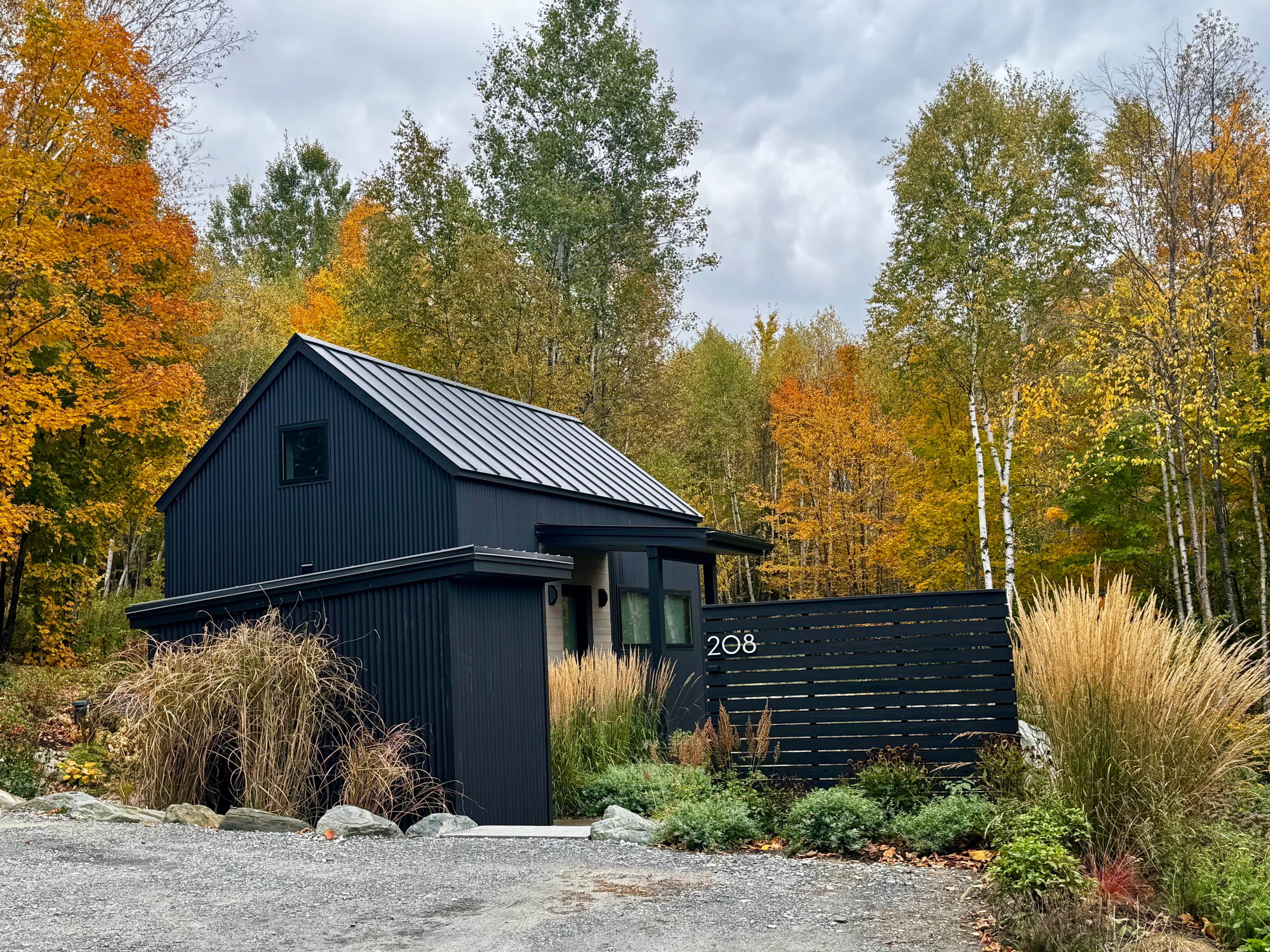 A modern black building with a metal roof, surrounded by autumn foliage and a gravel driveway.