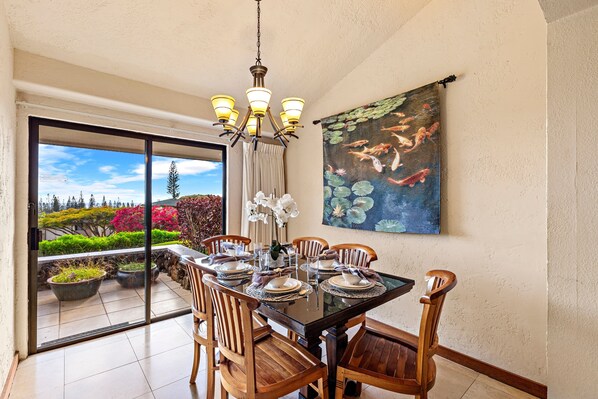 A dining area with a glass door leading to a garden, wooden chairs, a black table, and a chandelier.