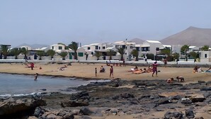 Een strand met mensen, een rotsachtige kustlijn en witte gebouwen op de achtergrond.