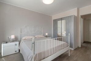 Un dormitorio con una cama de metal blanco, una mesita de noche con lámpara y un armario con espejo.