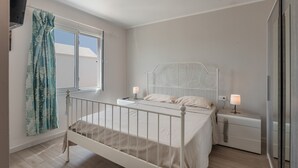 Een slaapkamer met een bed, nachtkastjes, een raam met gordijnen en een kledingkast.