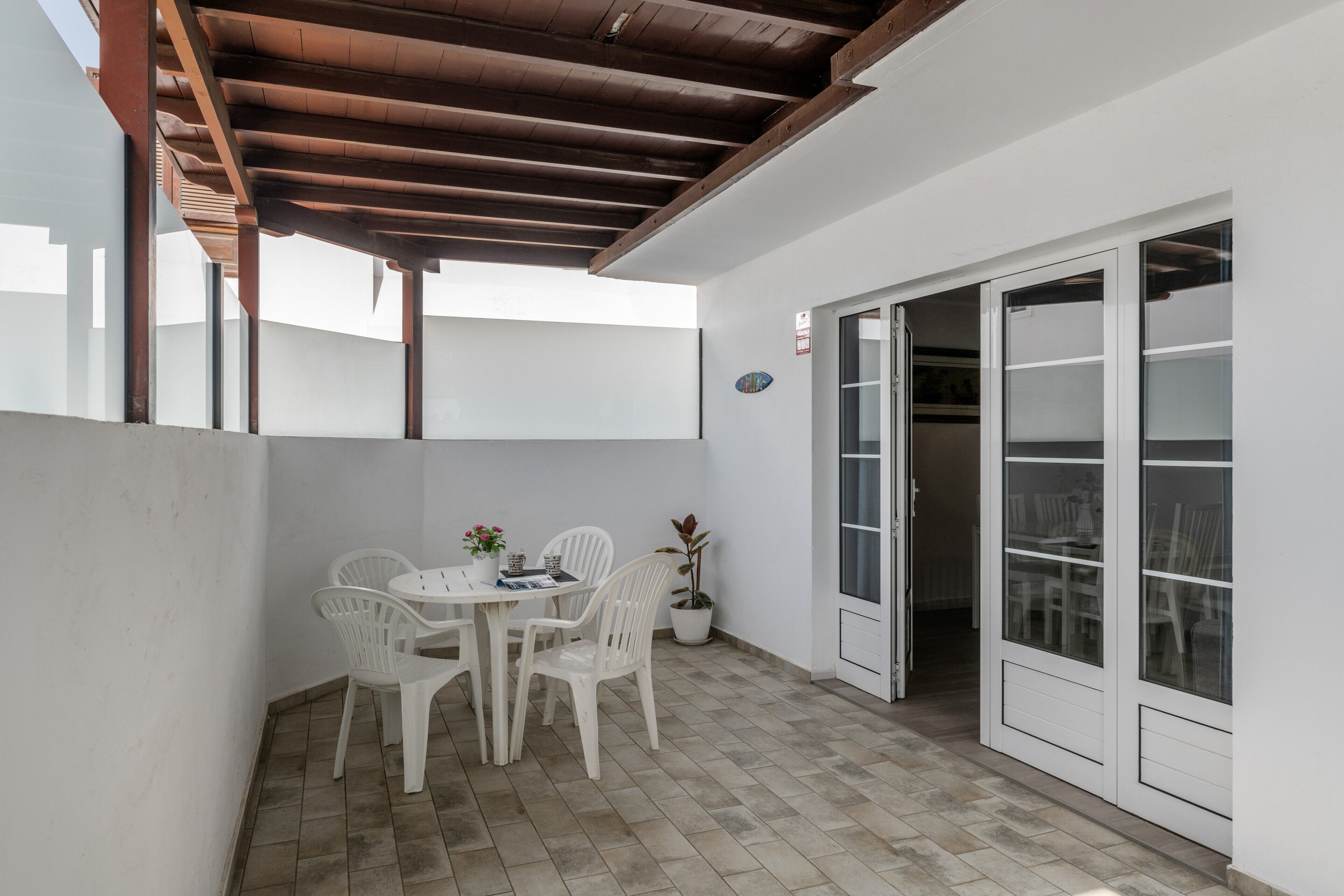 A covered patio area with a table and chairs, a potted plant, and a sliding glass door leading to an interior space.