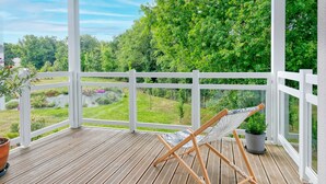 Una terraza de madera con una hamaca y plantas en macetas, con vistas a un paisaje verde y exuberante.