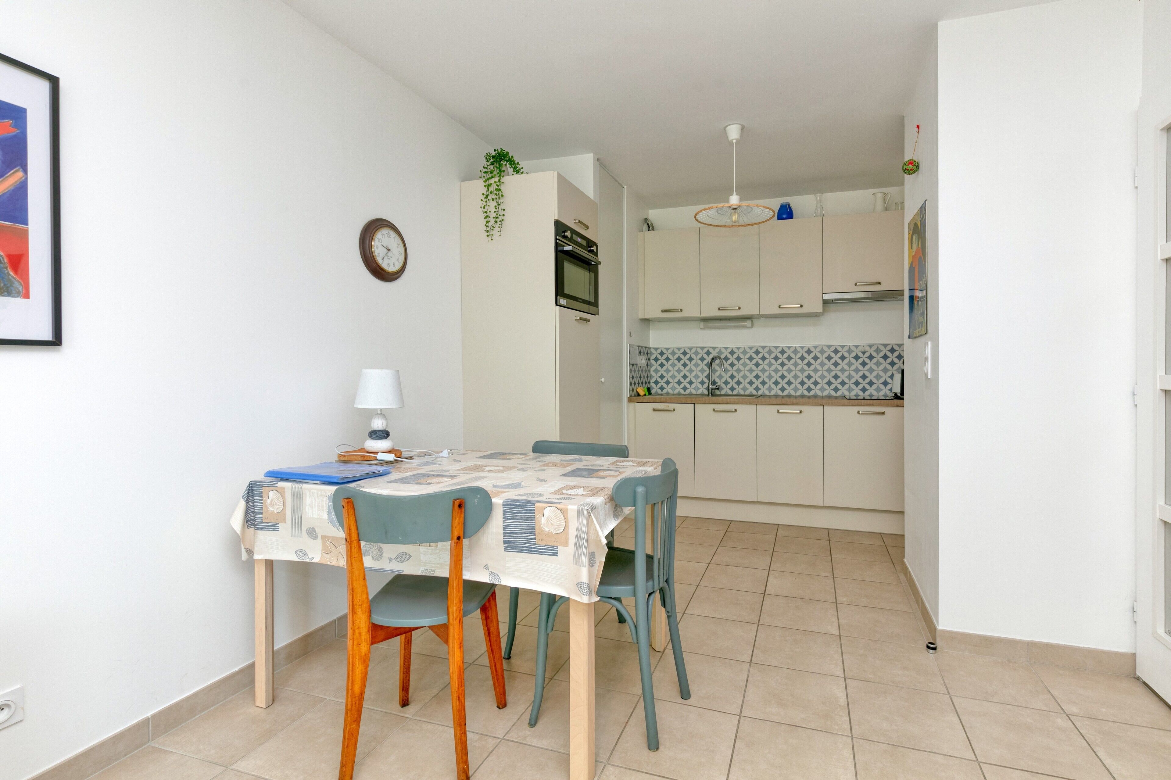 Une table à manger avec des chaises, une horloge et un coin cuisine avec des placards et un pare-feu en carreaux.