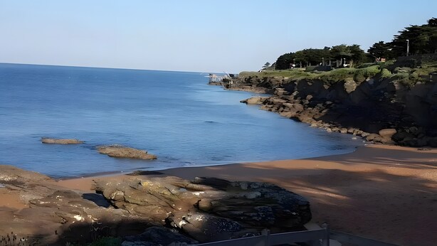 Un paisaje costero con una playa arenosa, un litoral rocoso y cielo despejado.