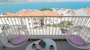 A balcony with two wicker chairs, a small table with two cups and a flower vase, and a view of the sea and buildings. - Trogir Stylish Apartment With Balcony and Sea View (Trogir)