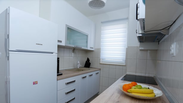 A modern kitchen with white cabinetry, a built-in microwave, and a fruit bowl on the counter. - Trogir Stylish Apartment With Balcony and Sea View (Trogir)