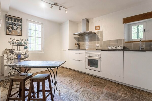 A kitchen with white cabinets, a stove, a window, and a metal rack with dishes.