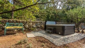 A stone wall, a bench, a hot tub, and a wooden deck in a forested area.