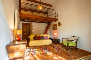 A room with a bed, a chair, a wooden bench, a lamp, a rug, and a staircase.