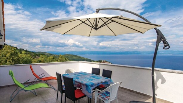 Une terrasse avec une table et des chaises, un parasol et une vue sur la mer.