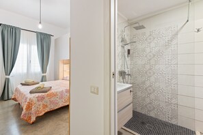 A bedroom with a bed, curtains, and a bathroom with a shower and patterned tiles.