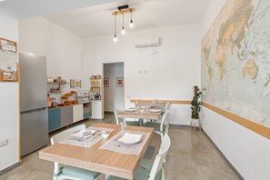 A modern dining area with wooden tables and chairs, a kitchen in the background, and a world map on the wall.