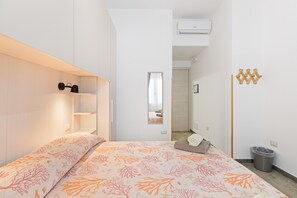 Une chambre à coucher comprenant un lit, une table de chevet, un miroir, une armoire et une poubelle.