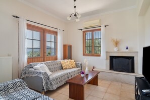 A living room with a sofa, a coffee table, a fireplace, and large windows. - Villa 'Melikokia' with Sea View, Wi-Fi and Air Conditioning (Unknown)