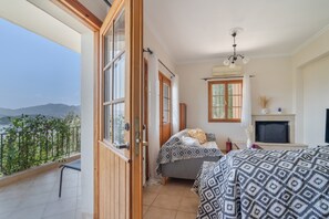 A bedroom with a balcony, a fireplace, and a view of the mountains. - Villa 'Melikokia' with Sea View, Wi-Fi and Air Conditioning (Unknown)