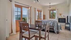 A room with a dining table, chairs, a bed with patterned bedding, a fireplace, and a television. - Villa 'Melikokia' with Sea View, Wi-Fi and Air Conditioning (Unknown)