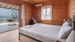 A wooden cabin bedroom with two beds, a desk, a chair, and a balcony with a hanging chair. - Villa 'Melikokia' with Sea View, Wi-Fi and Air Conditioning (Unknown)