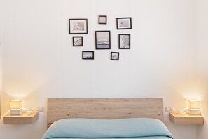 Een slaapkamer met een houten hoofdbord, een bed met een lichtblauwe deken, nachtkastjes met lampen, en een muur versierd met ingelijste foto’s.