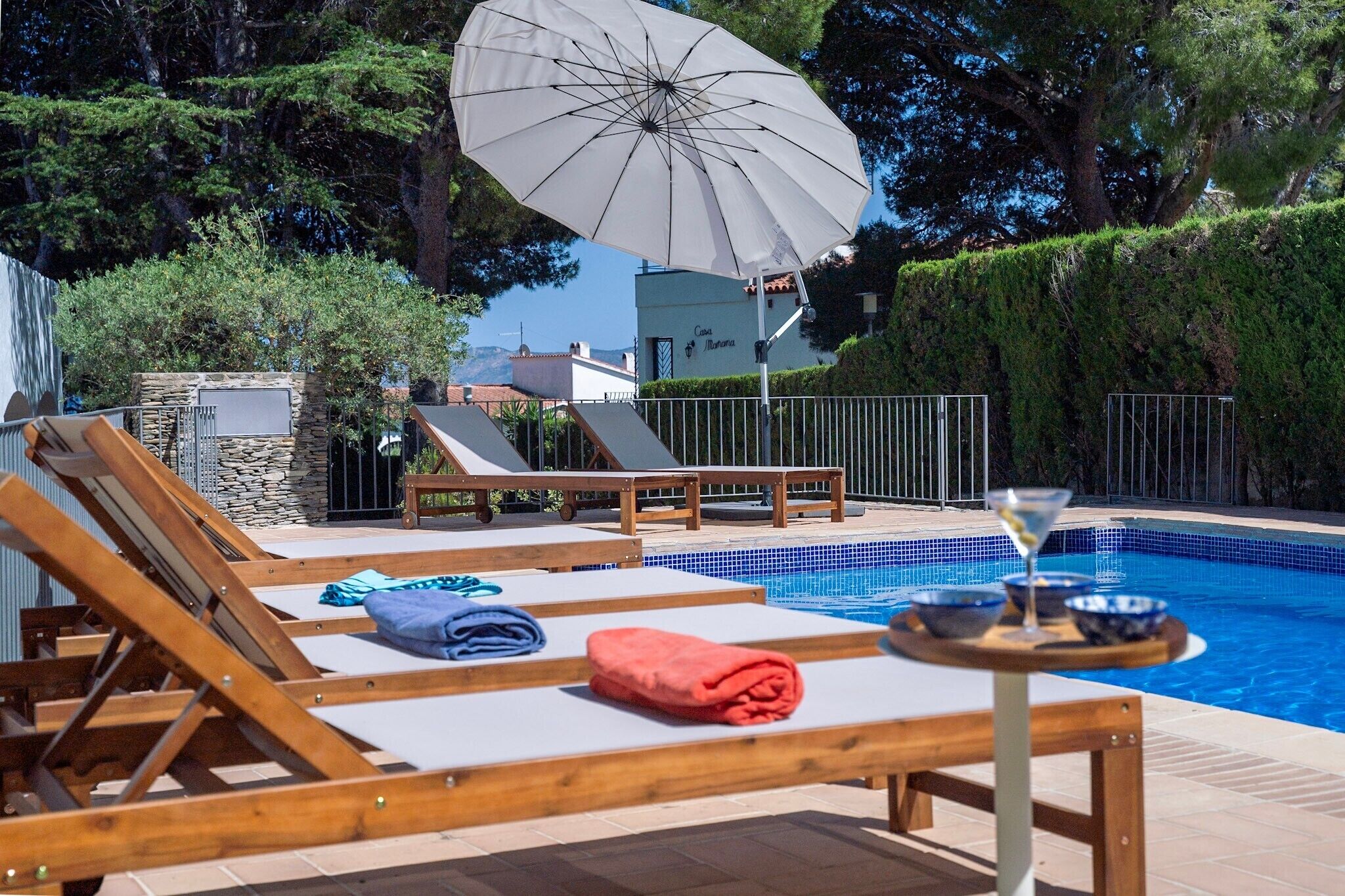 A poolside area with lounge chairs, a table with a drink, and a large umbrella.