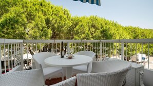 A balcony with white wicker furniture, a round table, and a bottle of wine. - Oasis 38: Pool, Private Parking, Steps from the Beach (Lido di Jesolo)