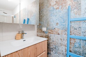 Een badkamer met een wit wastafel, houten kastje, blauwe handdoekhouder en douche.
