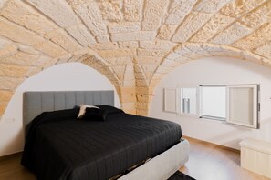 Een slaapkamer met een stenen plafond, een bed met een grijs hoofdeinde, en een witte nachtkastje.
