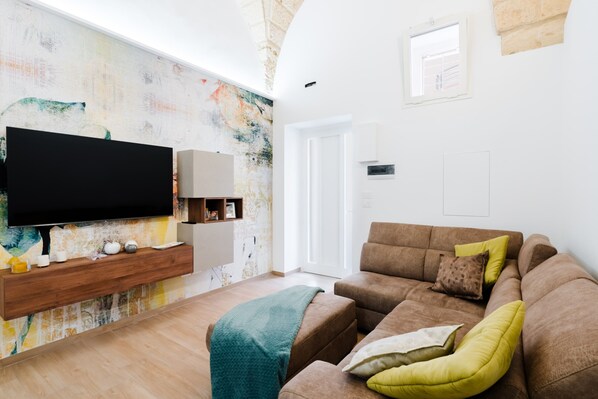 Een woonkamer met een flatscreen televisie, een houten console, een bruine bank en een kleurrijke abstracte wand.