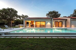 Uma casa moderna com piscina, um pátio com cadeiras de descanso e um gramado bem cuidado.