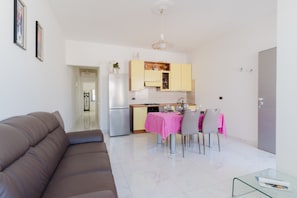Un salon moderne avec un canapé marron, une table basse en verre et un coin repas agrémenté d’une nappe rose.