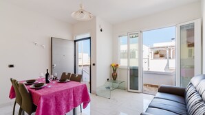 A dining area with a table set for four, a sofa, and a glass partition. - Holiday Home 'Casa 406' with Balcony and Air Conditioning (Torre San Giovanni)