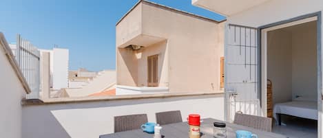 A rooftop terrace with a table set for two, a small window, and a door leading to a bedroom.