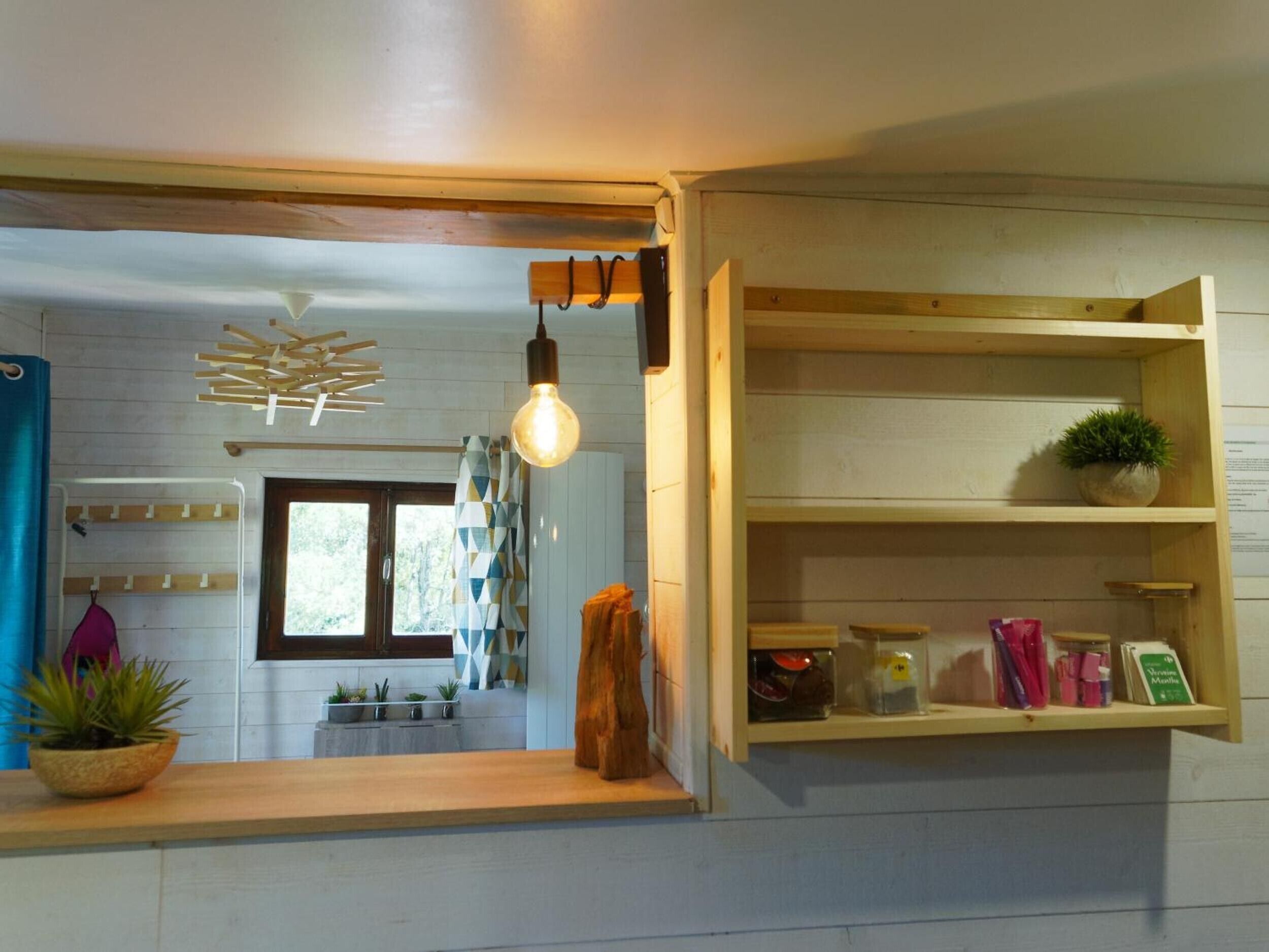 Una cucina con scaffali in legno, una lampadina a sospensione e una finestra.