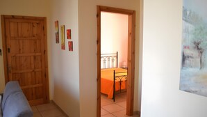 Una habitación con puerta de madera, una cama con colcha naranja y un cuadro en la pared.