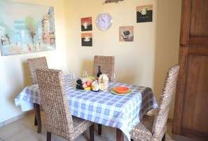Un coin repas avec une nappe à carreaux, des chaises en osier, une horloge et des œuvres d’art murales représentant du café.