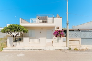 A two-story residential building with a balcony, a tree, and a flower pot.