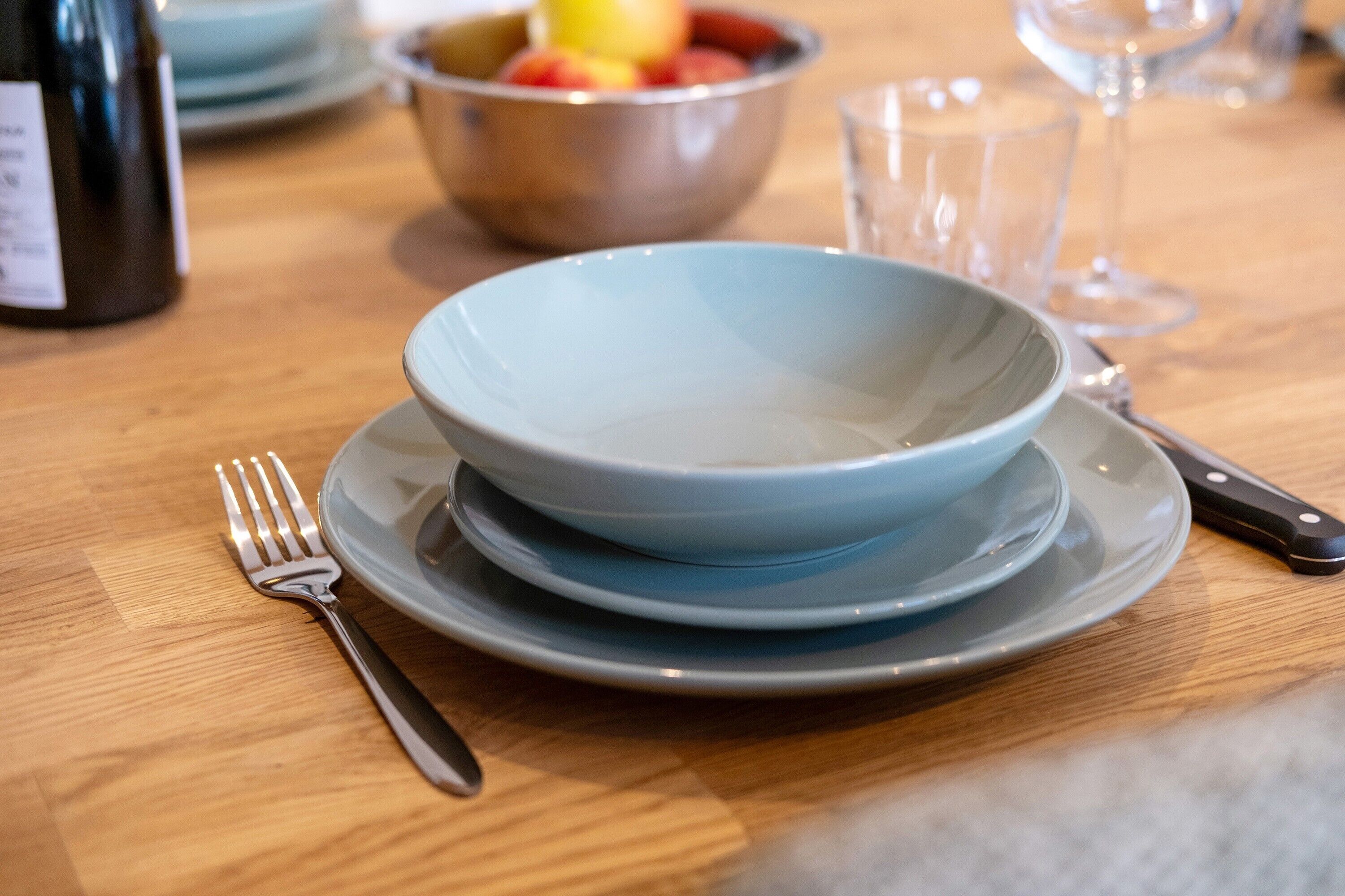 Una mesa de comedor con un bol, plato, tenedor, cuchillo y una botella de vino.