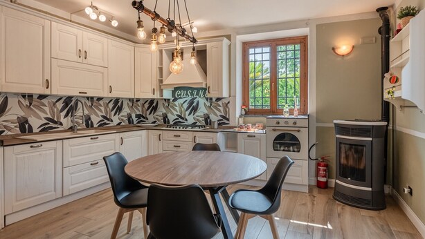 A kitchen with white cabinets, a round wooden table, black chairs, a gas stove, and a wood-burning stove.