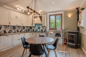 A kitchen with white cabinets, a round wooden table, black chairs, a gas stove, and a wood-burning stove. - House with private garden, pool, playground, free Wi-Fi – 30 minutes from the sea (Capannori)