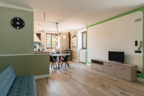 Een moderne woonkamer met een bank, een eethoek met een tafel en stoelen, een televisie op een kast, en een keuken op de achtergrond.